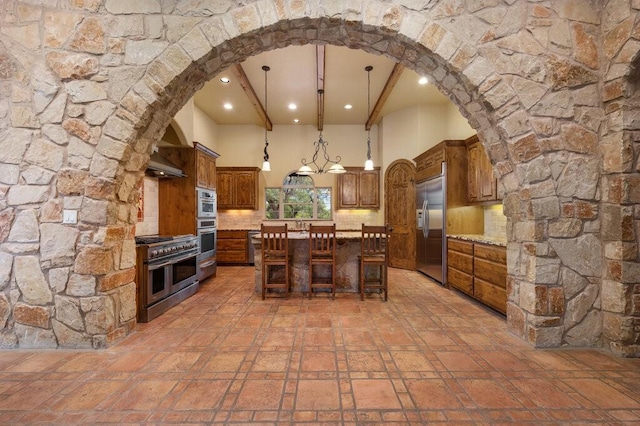 kitchen with tasteful backsplash, hanging light fixtures, premium appliances, a kitchen island, and beamed ceiling