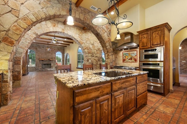 kitchen featuring wall chimney exhaust hood, light stone counters, a center island, pendant lighting, and black electric stovetop