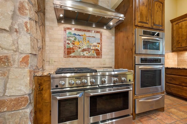 kitchen with stainless steel appliances, tasteful backsplash, light stone countertops, and exhaust hood