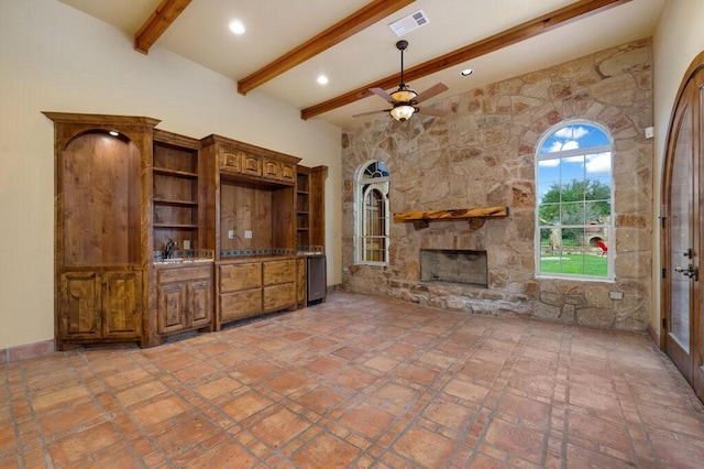 unfurnished living room with ceiling fan, a stone fireplace, sink, and beam ceiling