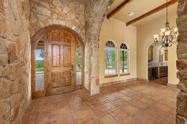 entrance foyer featuring a notable chandelier, a towering ceiling, beverage cooler, and beamed ceiling