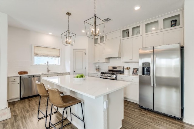 kitchen with sink, appliances with stainless steel finishes, a center island, decorative light fixtures, and custom exhaust hood