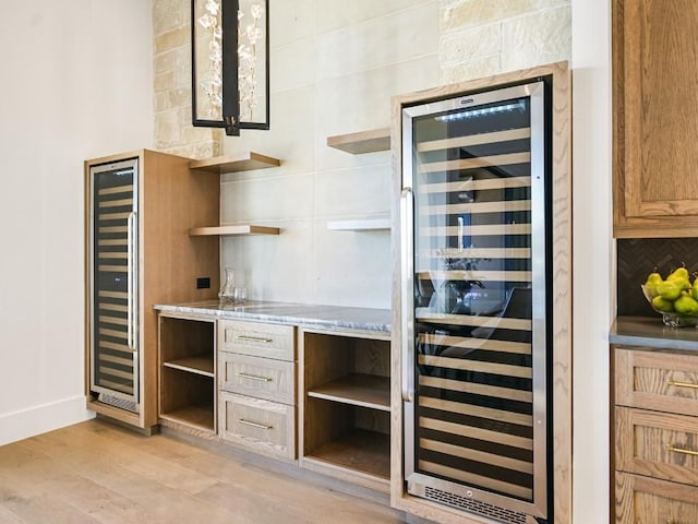 bar with light stone counters, decorative backsplash, light hardwood / wood-style flooring, and beverage cooler