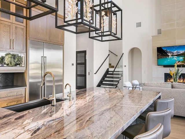 kitchen with a towering ceiling, sink, a breakfast bar area, stainless steel built in fridge, and light stone counters