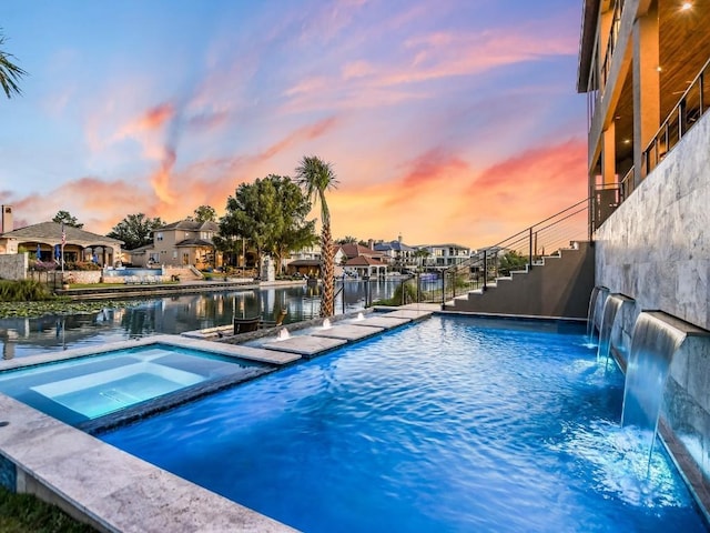 pool at dusk with an in ground hot tub, a water view, and pool water feature