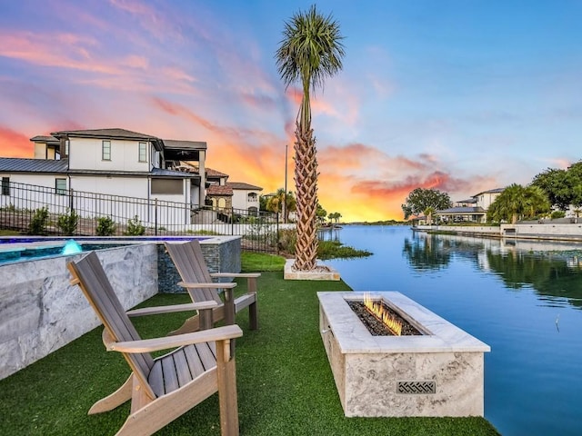 exterior space featuring a water view, a lawn, and a fire pit