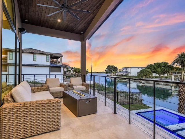 balcony at dusk featuring a water view, ceiling fan, and an outdoor living space with a fire pit