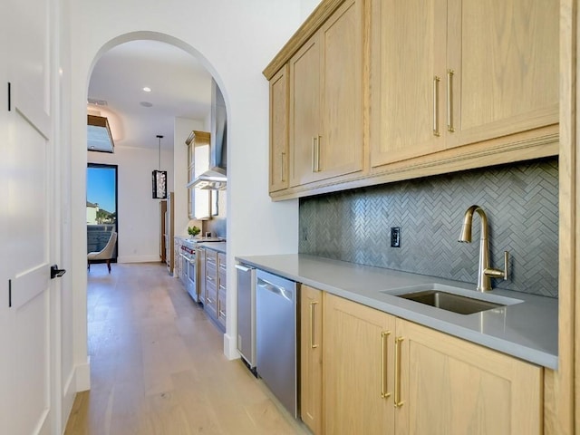 kitchen with appliances with stainless steel finishes, decorative light fixtures, sink, light brown cabinets, and wall chimney exhaust hood