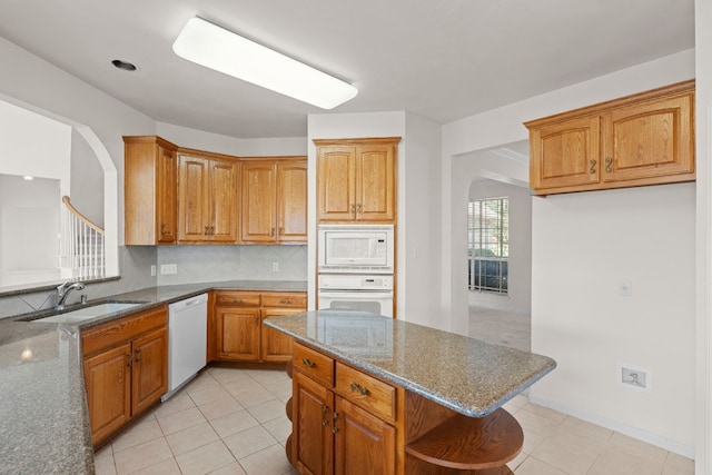 702 Timarron Dr, Leander, TX 78641 - kitchen featuring white appliances, dark stone countertops, arched walkways, open shelves, and light tile patterned floors