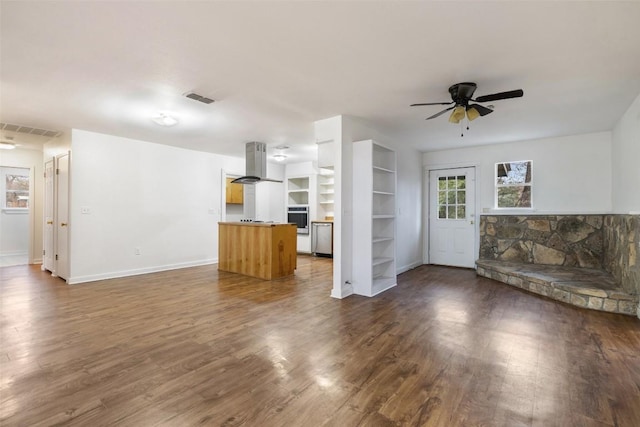 unfurnished living room featuring built in shelves, ceiling fan, and dark hardwood / wood-style floors