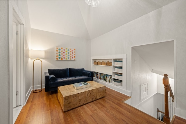 living room featuring wood-type flooring, vaulted ceiling, and built in shelves