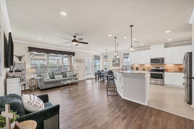 kitchen with pendant lighting, a breakfast bar area, white cabinets, stainless steel appliances, and a center island with sink