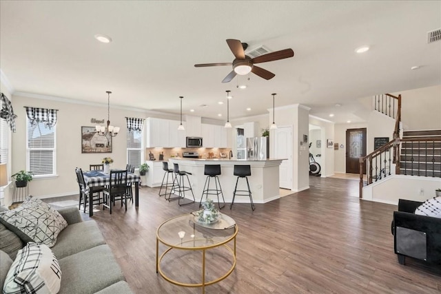 living room featuring ceiling fan with notable chandelier, ornamental molding, and dark hardwood / wood-style floors