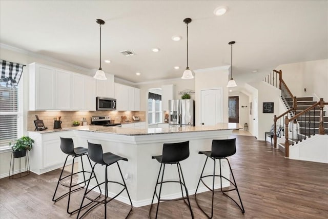 kitchen featuring stainless steel appliances, tasteful backsplash, white cabinets, decorative light fixtures, and a large island with sink