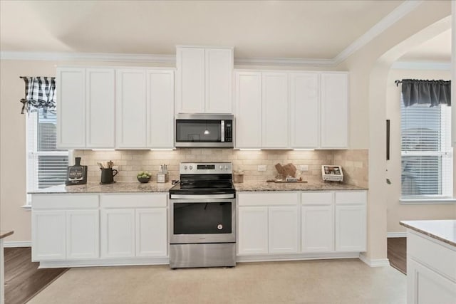 kitchen with white cabinetry, ornamental molding, appliances with stainless steel finishes, light stone countertops, and backsplash