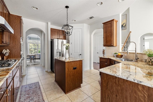 kitchen with sink, appliances with stainless steel finishes, a center island, light stone countertops, and decorative light fixtures