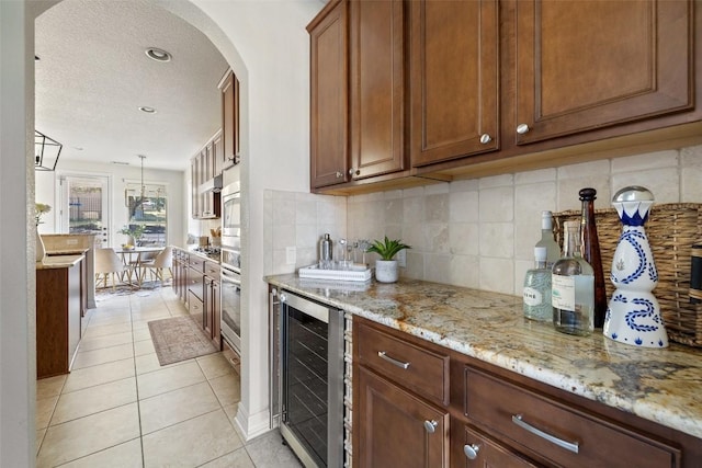 kitchen with pendant lighting, light tile patterned floors, wine cooler, light stone counters, and tasteful backsplash