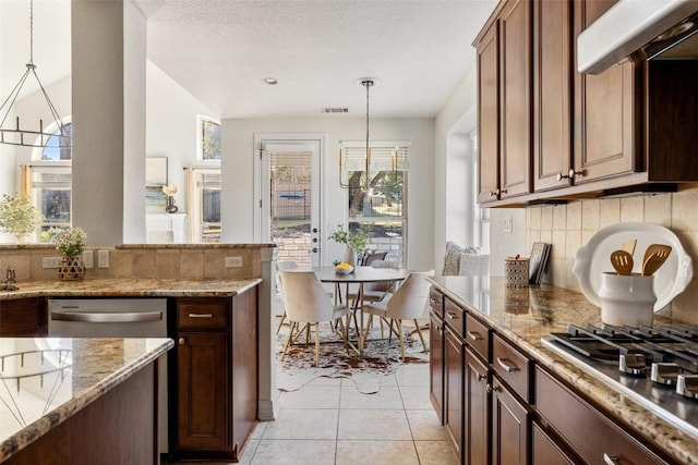 kitchen with appliances with stainless steel finishes, light stone countertops, a healthy amount of sunlight, and decorative light fixtures