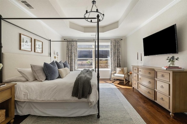 bedroom with dark wood-type flooring, a notable chandelier, a tray ceiling, and crown molding