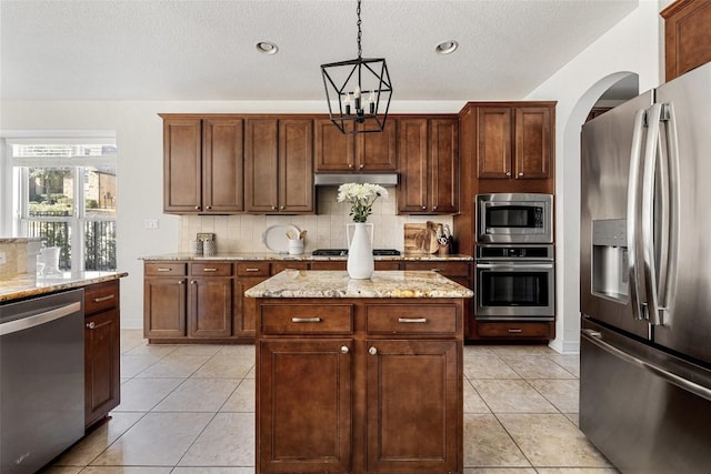 kitchen with stainless steel appliances, light stone countertops, hanging light fixtures, and a center island