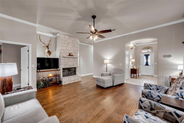 living room with ceiling fan, a stone fireplace, ornamental molding, and light wood-type flooring