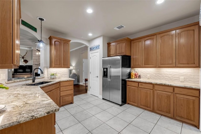 kitchen with sink, stainless steel fridge, light stone countertops, decorative backsplash, and decorative light fixtures