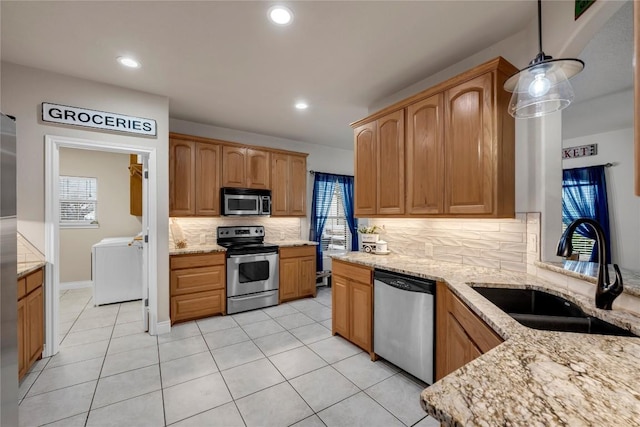 kitchen with sink, hanging light fixtures, stainless steel appliances, light stone counters, and washer and dryer