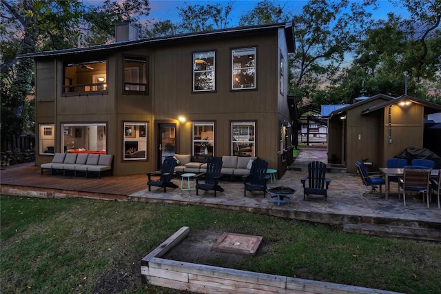 back house at dusk featuring a wooden deck, a storage unit, an outdoor living space, and a lawn