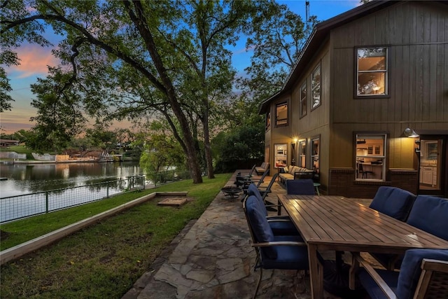 patio terrace at dusk featuring a yard, an outdoor hangout area, and a water view