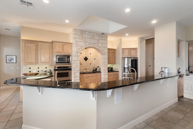 5019 Mcintyre Cir, Austin, TX 78734 - kitchen with stainless steel appliances, light brown cabinetry, decorative backsplash, light tile patterned floors, and a kitchen breakfast bar