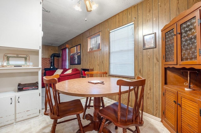 dining area featuring a healthy amount of sunlight, a wood stove, a textured ceiling, and wooden walls