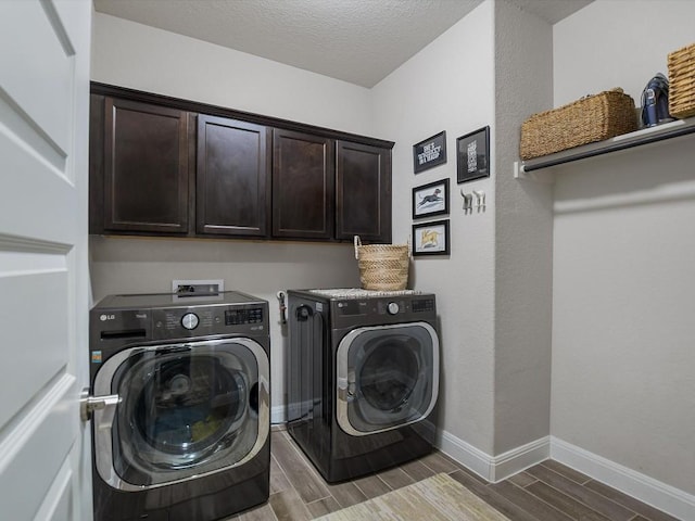 laundry area featuring a textured ceiling, wood finish floors, baseboards, cabinet space, and washer and clothes dryer