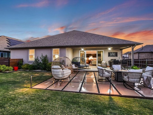 back of house at dusk featuring a lawn, fence, an outdoor living space, and stucco siding