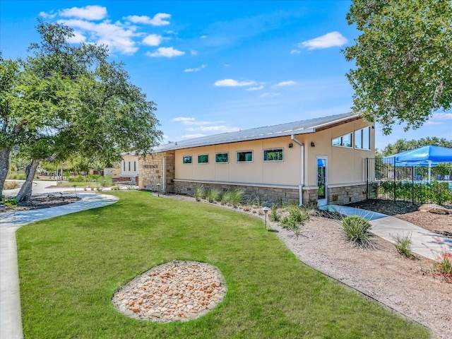 rear view of house featuring stone siding, a yard, and stucco siding