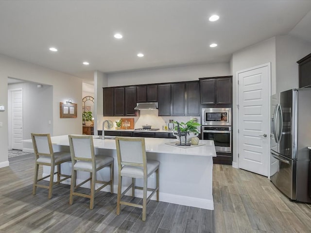 kitchen featuring stainless steel appliances, recessed lighting, light countertops, light wood-style floors, and under cabinet range hood