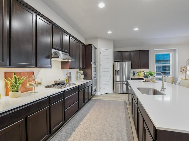 kitchen with a center island with sink, stainless steel appliances, light countertops, a sink, and under cabinet range hood