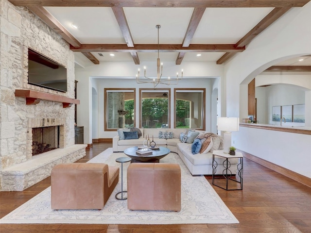 living room with hardwood / wood-style flooring, a stone fireplace, a chandelier, and beamed ceiling