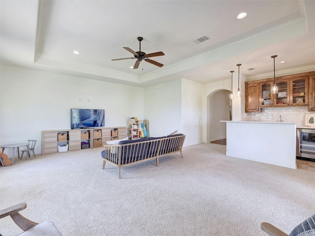 living room featuring a tray ceiling, light colored carpet, beverage cooler, and ceiling fan