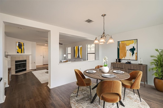 dining space with a tile fireplace, dark wood-type flooring, and a notable chandelier