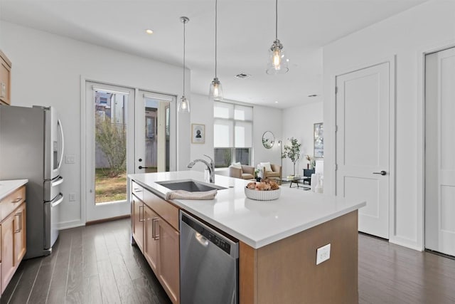 kitchen with hanging light fixtures, appliances with stainless steel finishes, a kitchen island with sink, and dark hardwood / wood-style flooring