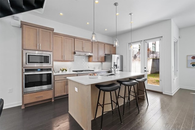 kitchen featuring an island with sink, sink, backsplash, hanging light fixtures, and stainless steel appliances