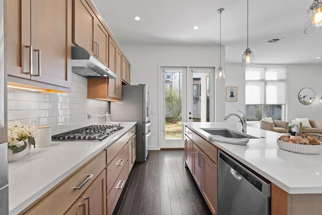 kitchen with sink, a center island with sink, pendant lighting, stainless steel appliances, and decorative backsplash