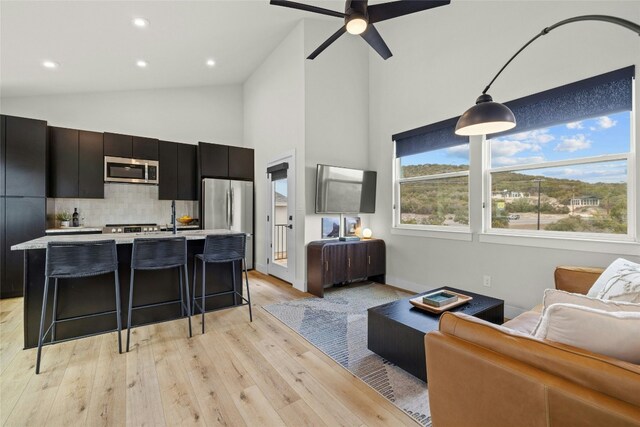 kitchen with a breakfast bar, pendant lighting, an island with sink, stainless steel appliances, and light hardwood / wood-style flooring