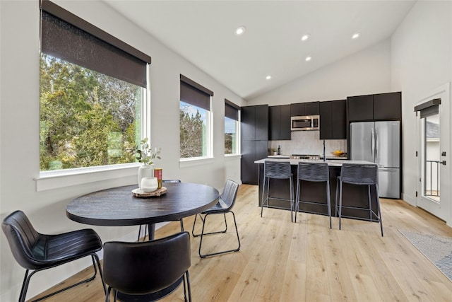 kitchen with appliances with stainless steel finishes, a breakfast bar, a wealth of natural light, and light hardwood / wood-style floors