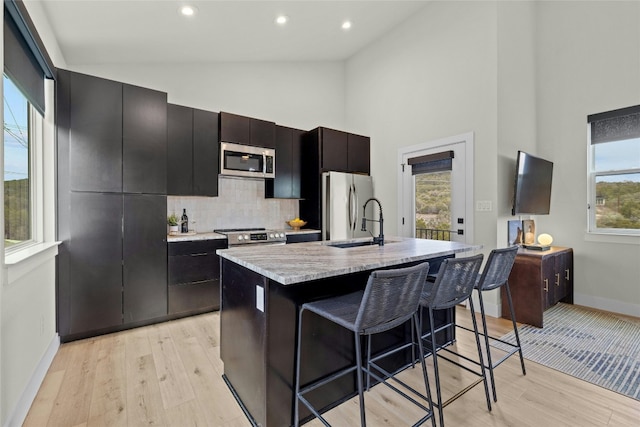 kitchen with appliances with stainless steel finishes, tasteful backsplash, an island with sink, a breakfast bar area, and light hardwood / wood-style flooring