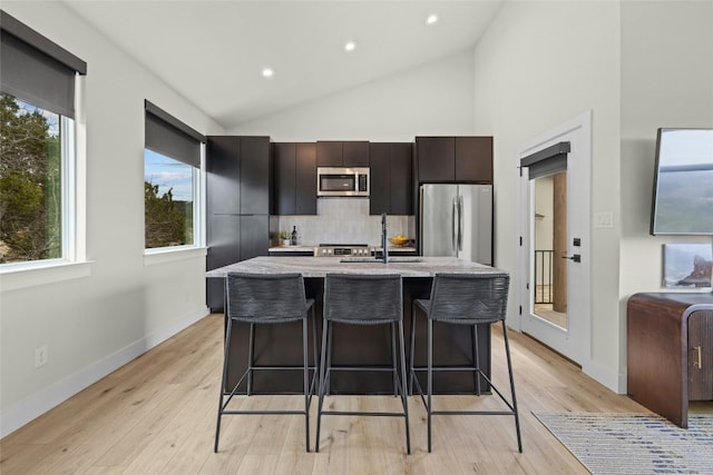 kitchen featuring light wood-style flooring, stainless steel appliances, a sink, a kitchen breakfast bar, and a center island with sink