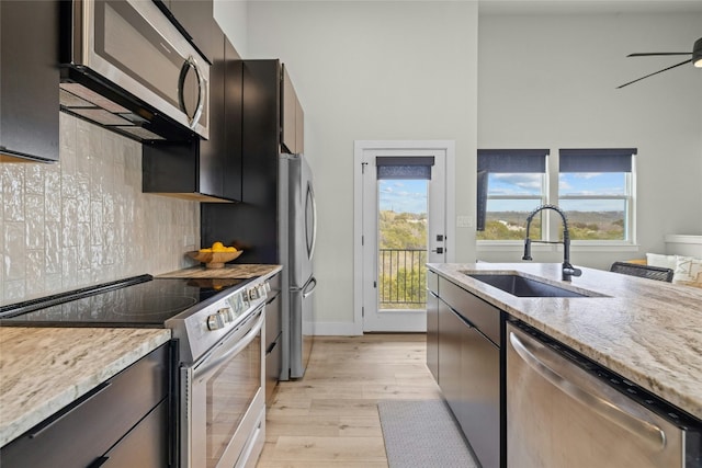 kitchen featuring tasteful backsplash, ceiling fan, appliances with stainless steel finishes, light wood-style floors, and a sink