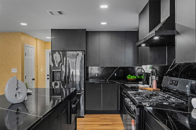 kitchen with wall chimney range hood, sink, light hardwood / wood-style flooring, backsplash, and gas stove