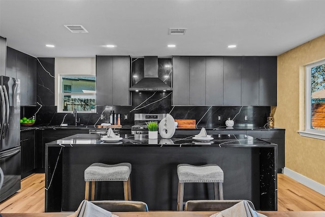 kitchen with wall chimney exhaust hood, stainless steel range oven, sink, black refrigerator, and a kitchen island