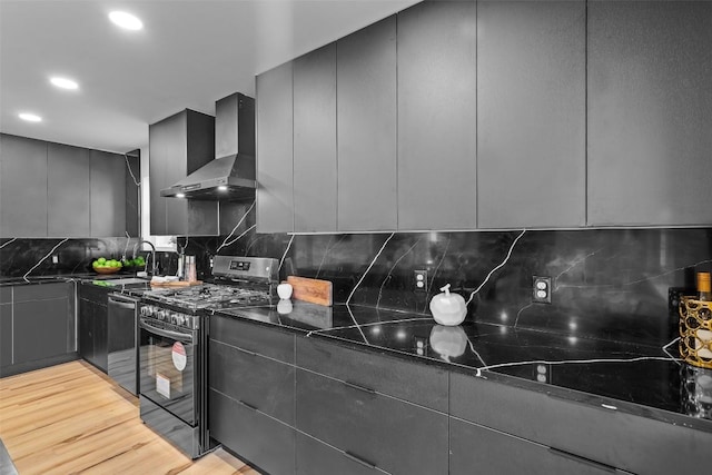 kitchen featuring sink, light hardwood / wood-style flooring, dark stone counters, stainless steel appliances, and wall chimney range hood